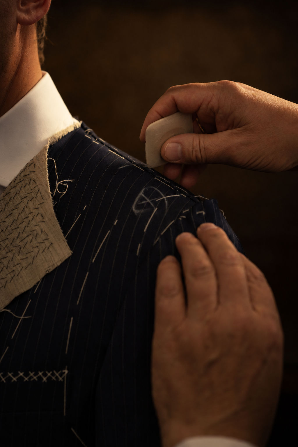 Tailor marking tailor's chalk on the shoulder of a basted navy pinstripe jacket during a fitting